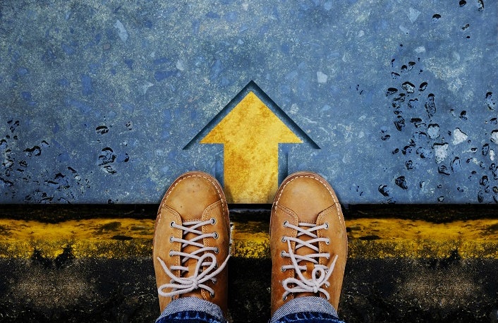 Upshot of 2 yellow shoes standing at an arrow pointing straight ahead