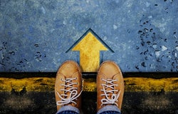 Upshot of 2 yellow shoes standing at an arrow pointing straight ahead