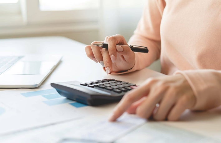 Person sitting at a desk making calculations on a calculator while holding a pen