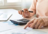 Person sitting at a desk making calculations on a calculator while holding a pen