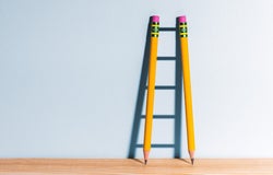 Two pencils creating a shadow of a ladder against a wall