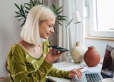 gen z female working on laptop and talking on mobile phone in her room