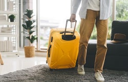 People getting ready for holidays travel trip concept. Single traveller man walking carry a luggage begin a journey. Men wear casual cloth and sneakers. Background in living room at home or hotel.