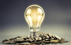 Shining lightbulb standing upright in a heap of coins