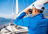 Young man captain on the yacht looking through binoculars during sailing boat control. Travel and active life.