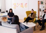 People sitting on sofas and chairs in a modern office in front of a whiteboard